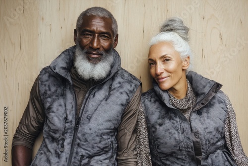 Portrait of a happy multiethnic couple in their 60s dressed in a water-resistant gilet isolated on light wood minimalistic setup