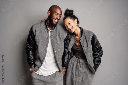 Portrait of a glad mixed race couple in their 30s sporting a stylish varsity jacket isolated in blank studio backdrop