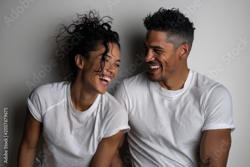 Portrait of a joyful latino couple in their 30s dressed in a casual t-shirt while standing against plain cyclorama studio wall