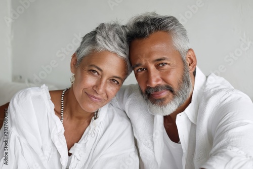 Portrait of a content latino couple in their 60s wearing a classic white shirt on crisp minimalistic living room