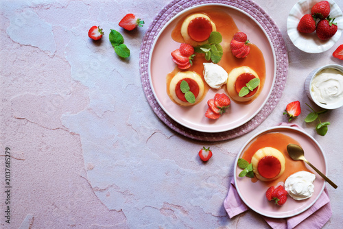 Crème caramel classic French custard dessert topped with a layer of soft caramel sauce and served with strawberries, apple mint and whipped cream. Horizontal with negative copy space.