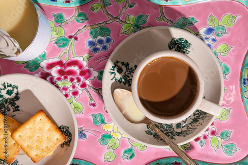 Kopi with condensed milk and crackers on a vibrant floral tray