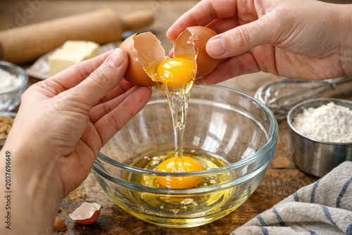 Close-up of egg being added to mixing bowl, symbolizing baking, recipe preparation, and culinary activity