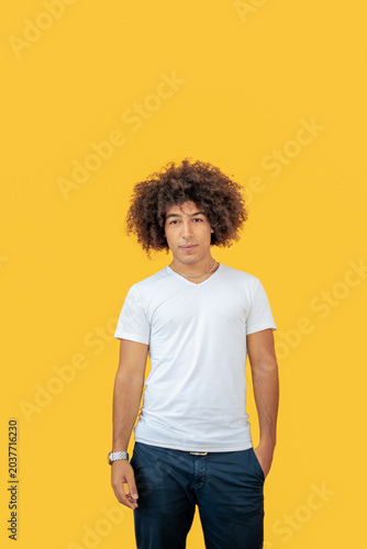 Beautiful young mixed race men with thick curly hair on a yellow background. Multiethnic Afro italian male looking away, sincere eyes, dressed in a white T-shirt and jeans, isolated