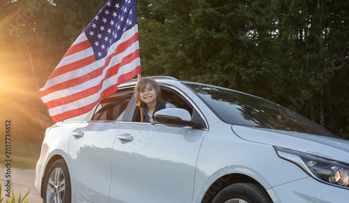 An American flag on a car and a happy child looking out the window on Independence Day. Celebrating a national holiday.   weekend getaway. A bright future.