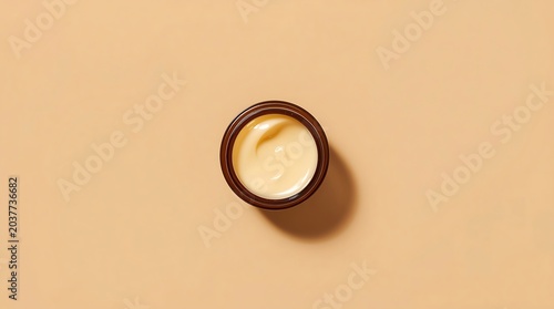 Top-Down View of a Small, Open Jar of Creamy Skincare Product on a Beige Surface.