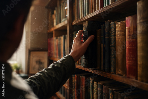 Person reaching for a book on high wooden bookshelf