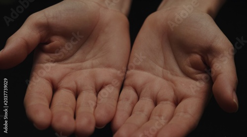 Human hands cup together against a dark background. Open palms face upward in a gentle gesture. Hands held open create a cupped shape. Palms face the sky in a receiving pose.