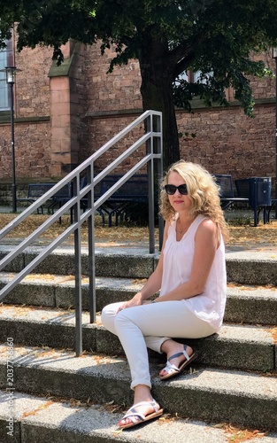 Curly-haired blonde in sunglasses sits on the steps