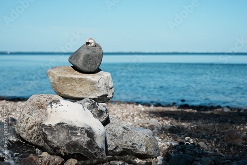 Canvas Print Stacked stones with a small seashell on a pebble beach by the calm blue sea