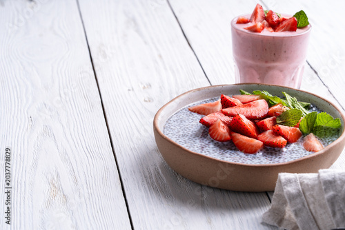 Chia seed pudding topped with sliced strawberry. Glass of strawberry smoothie on white wooden background