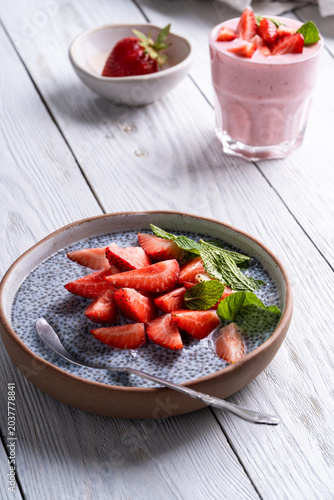 Chia seed pudding topped with sliced strawberry. Glass of strawberry smoothie on white wooden background