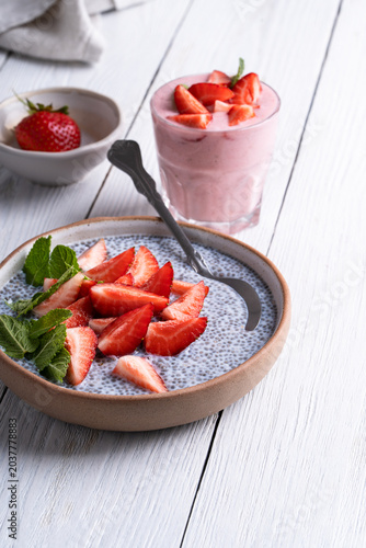 Chia seed pudding topped with sliced strawberry. Glass of strawberry smoothie on white wooden background