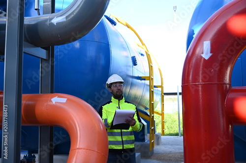 Industrial engineer inspecting large water treatment system equipment at a municipal water plant. Maintenance of pipelines, valves, pumps and storage tanks supporting clean water production and utilit