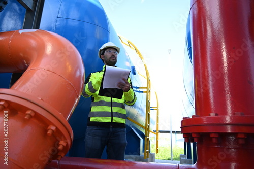 Industrial engineer inspecting large water treatment system equipment at a municipal water plant. Maintenance of pipelines, valves, pumps and storage tanks supporting clean water production and utilit