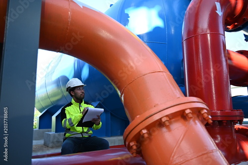 Industrial engineer inspecting large water treatment system equipment at a municipal water plant. Maintenance of pipelines, valves, pumps and storage tanks supporting clean water production and utilit
