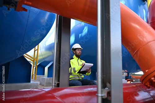 Industrial engineer inspecting large water treatment system equipment at a municipal water plant. Maintenance of pipelines, valves, pumps and storage tanks supporting clean water production and utilit