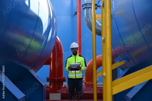 Industrial engineer inspecting large water treatment system equipment at a municipal water plant. Maintenance of pipelines, valves, pumps and storage tanks supporting clean water production and utilit