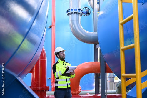 Industrial engineer inspecting large water treatment system equipment at a municipal water plant. Maintenance of pipelines, valves, pumps and storage tanks supporting clean water production and utilit
