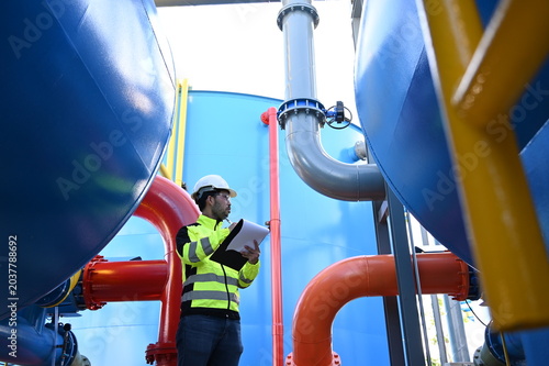 Industrial engineer inspecting large water treatment system equipment at a municipal water plant. Maintenance of pipelines, valves, pumps and storage tanks supporting clean water production and utilit
