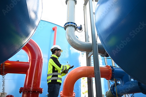 Industrial engineer inspecting large water treatment system equipment at a municipal water plant. Maintenance of pipelines, valves, pumps and storage tanks supporting clean water production and utilit