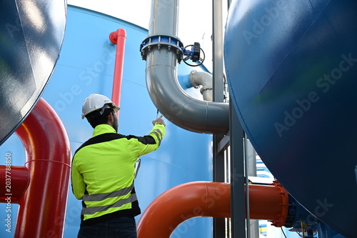 Industrial engineer inspecting large water treatment system equipment at a municipal water plant. Maintenance of pipelines, valves, pumps and storage tanks supporting clean water production and utilit