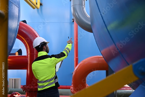 Industrial engineer inspecting large water treatment system equipment at a municipal water plant. Maintenance of pipelines, valves, pumps and storage tanks supporting clean water production and utilit