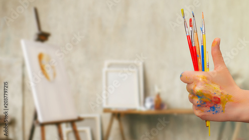 Artist holds paintbrushes with colorful paint on hand in studio during creative session
