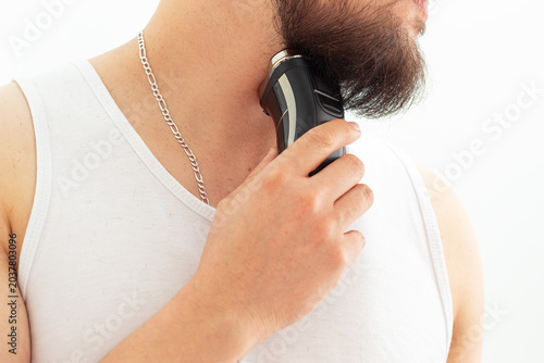 Young man trimming his beard with a rotary electric shaver during a home grooming routine