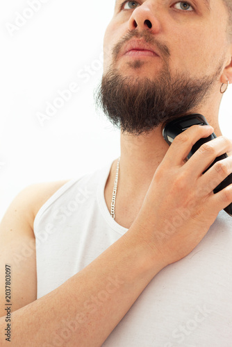 Man trimming his beard from the neck up with an electric shaver during a home grooming routine. Hygiene and personal appearance