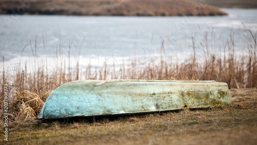Tableau sur toile Weathered turquoise boat rests upside down on grassy bank