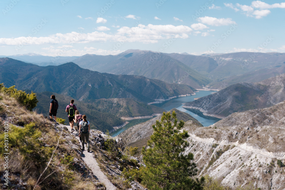 Obraz premium Group of hikers exploring a scenic mountain trail with panoramic views of rivers and valleys during a clear day