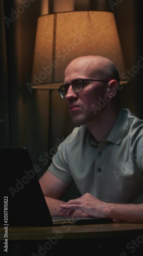 Man in glasses stock trader in home office. Male analyzes terminal, trades stocks on crypto market. Smartphone monitor and laptop display vivid candlestick chart, trading charts, price action. Evening