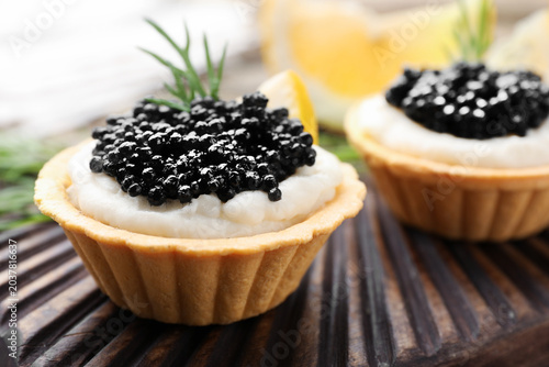 Fotografie Tasty tartlets with black caviar, cream cheese, dill and lemon on table, closeup