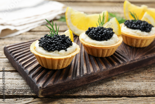 Obraz na płótnie Tasty tartlets with black caviar, cream cheese, dill and lemon on wooden table,