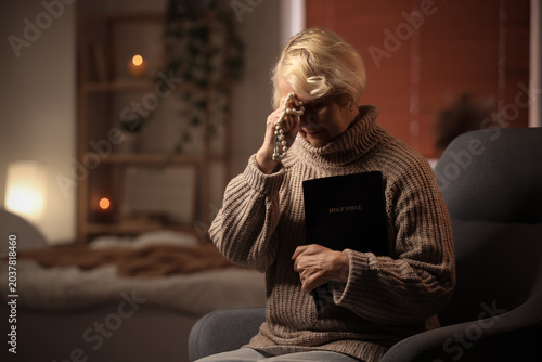 Картината върху платно Elderly woman praying with rosary and holding Holy Bible at home, senior Christi