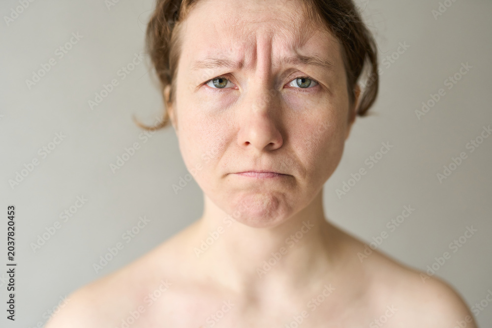 Fototapeta premium Woman Frowning Furrowed Brow Looking Directly At Camera With Bare Shoulders Neutral Background Soft Lighting Conveying Concern Or Dissatisfaction.
