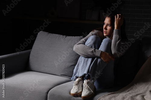 Scared young woman sitting on sofa at home