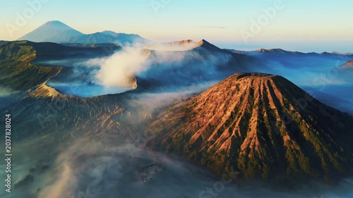 Cinematic aerial view of Mount Bromo volcano at sunrise – Breathtaking drone shot of morning mist covering the vast caldera and dramatic mountain peaks in East Java, Indonesia landscape 4k