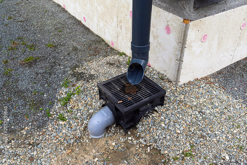 фотографія A black plastic drainage grate embedded in gravel collects rainwater from a dark
