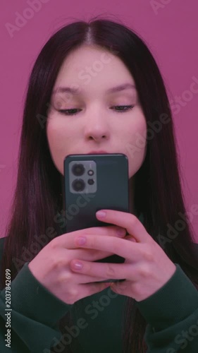 Portrait: young brunette woman with black hair, typing text on phone, schoolgirl. Closeup: young white kid using smartphone, texting. Teen girl use app social media. Teenager wear pullover in studio