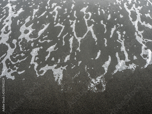 Obraz na plátne White sea foam traces on wet black volcanic sand beach