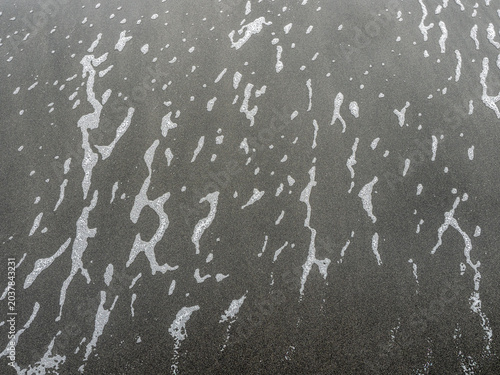 Φωτογραφία White sea foam traces on wet black volcanic sand beach