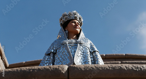 Woman in ornate costume with elaborate headwear looking up.