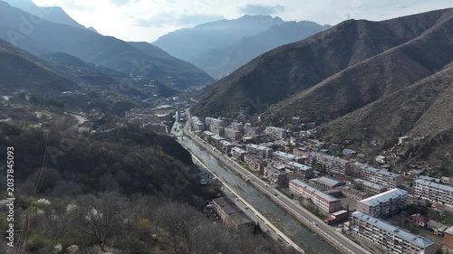 An aerial drone shot of a beautiful, scenic city nestled in a deep mountain valley with residential buildings, houses, and roads on a sunny day in Kapan, Armenia.

