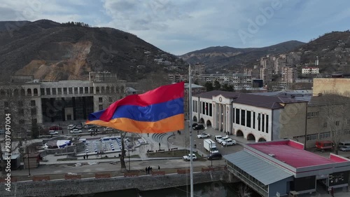 An aerial drone shot of a beautiful, scenic city nestled in a deep mountain valley with residential buildings, houses, and roads on a sunny day in Kapan, Armenia.

