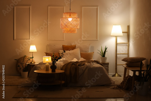 Foto Interior of stylish bedroom with cozy bed, houseplants and glowing lamps at nigh