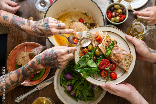 Photos Tattooed hands sharing a meal with salad, bread, and olives on a table