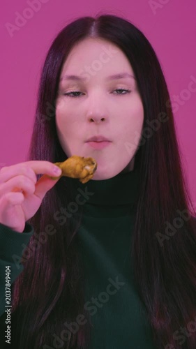 Teen girl eating fried chicken meat wings. Unhealthy fast street food snack, crispy junk. Protein lunch, high calories. Young woman biting nuggets. Youth culture and indulgence concept.