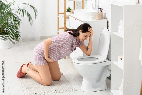 Quadro su tela Pregnant woman suffering from morning sickness and nausea kneeling by toilet in